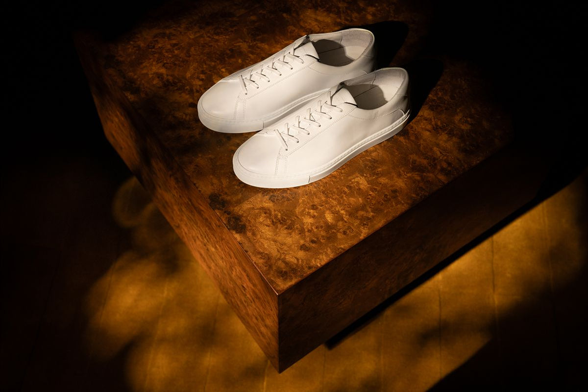 Angled view of the Capri Triple White low-top sneakers showcasing lace-up design on a dark wood table