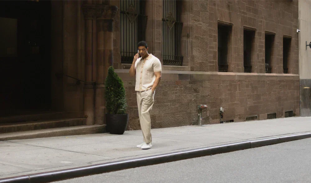 Man walking while talking on a phone in a cream smart-casual outfit with Capri Triple White sneakers on a city sidewalk