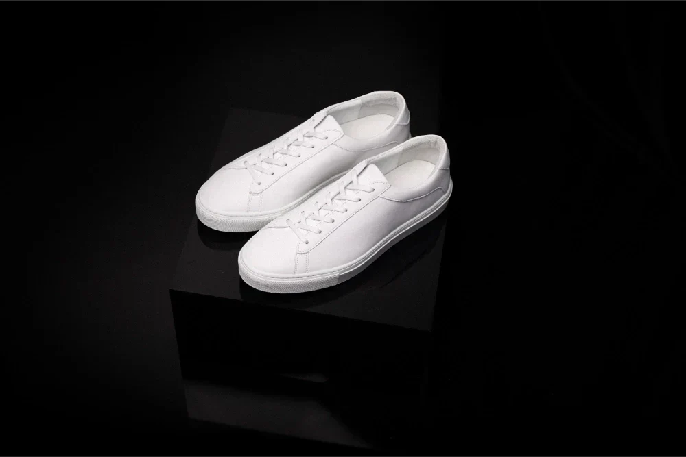 Angled view of Capri Triple White low-top sneakers showcasing minimalist design on a black pedestal