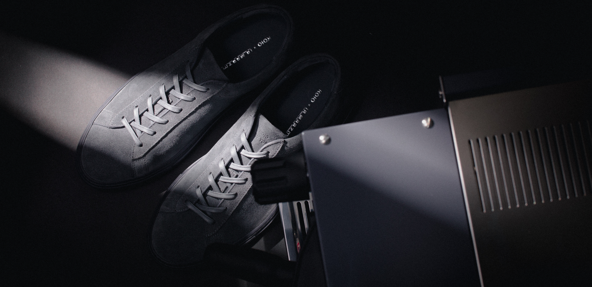 Top view of men’s grey suede low-top sneakers showcasing lace-up design beside a La Marzocco espresso machine