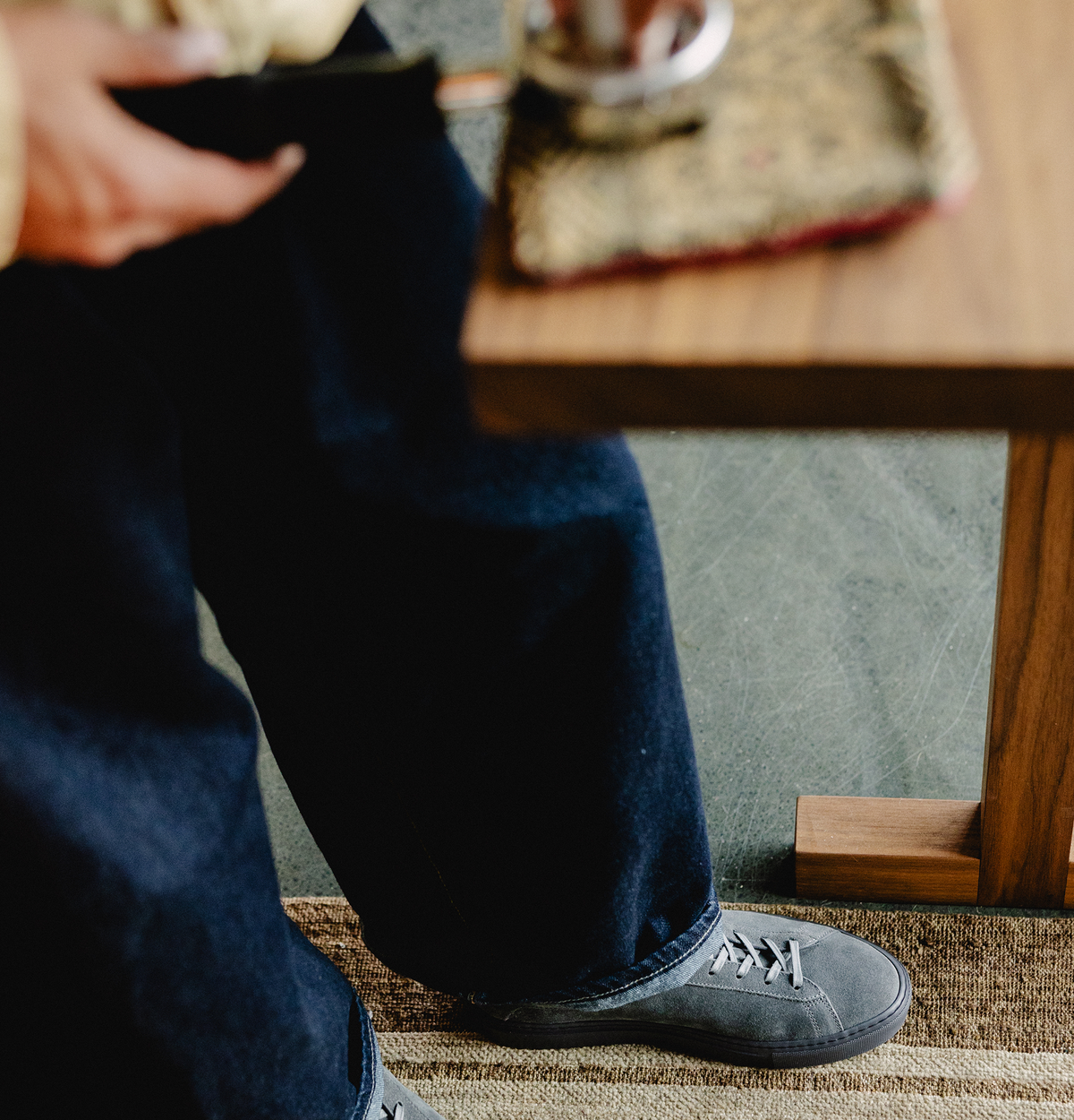 Side view of Koio x La Marzocco Capri low-top sneaker showcasing grey calf suede on a seated wearer indoors