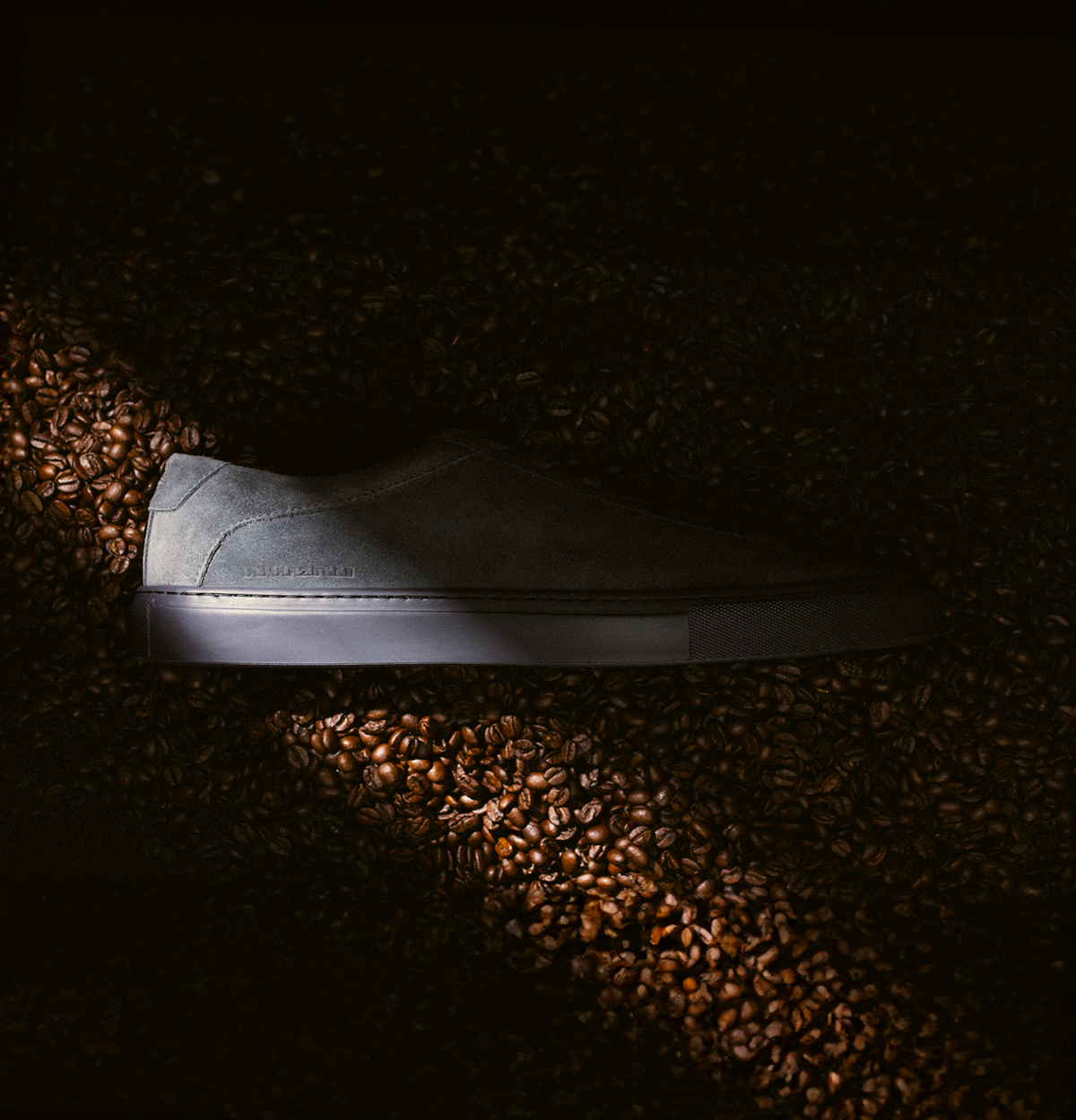 Side view of the Capri men’s grey suede low-top sneaker showcasing its dark rubber sole with coffee beans in the background