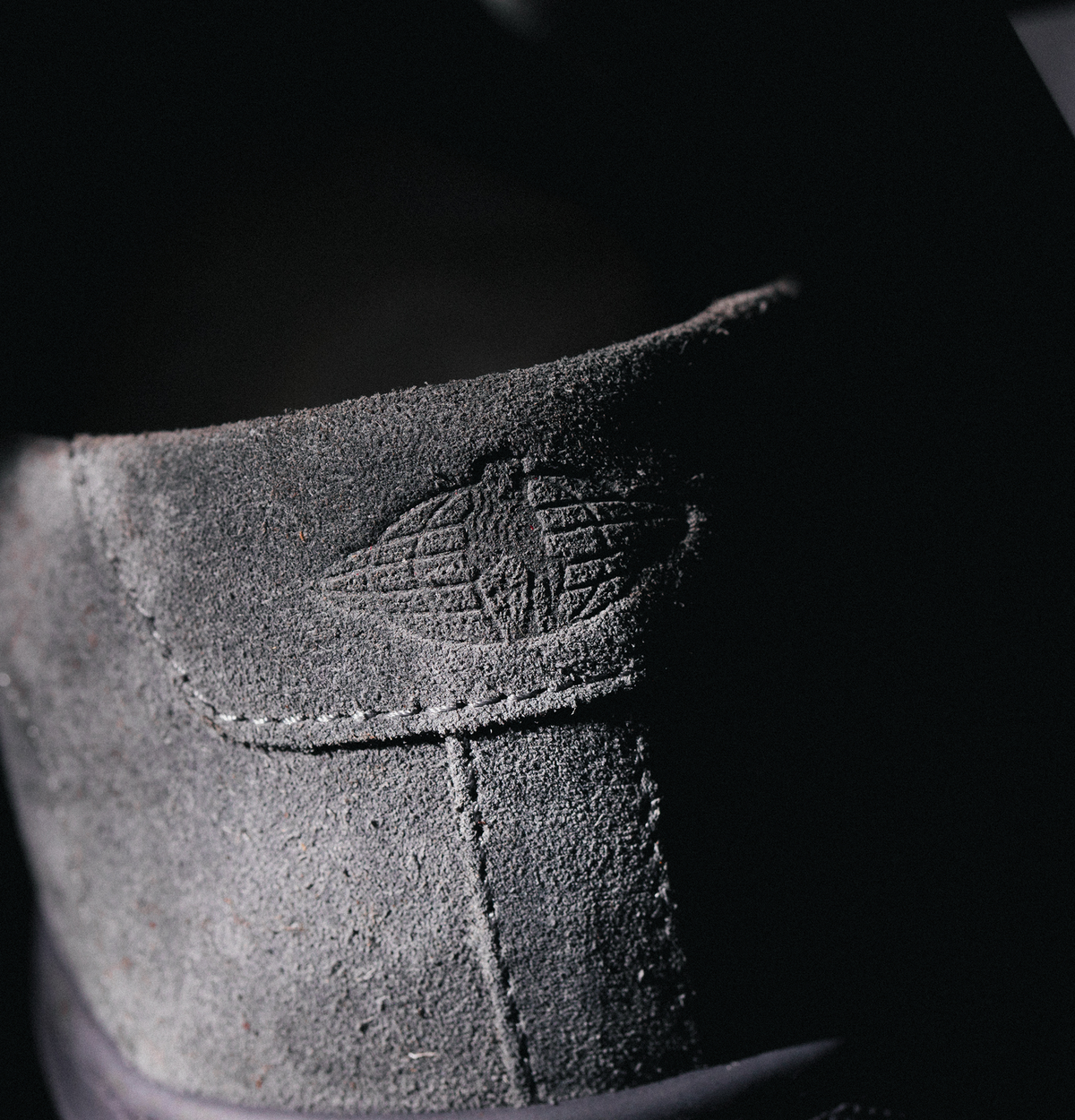 Close-up of the men’s grey suede low-top Capri sneaker showcasing textured suede and embossed side logo against black