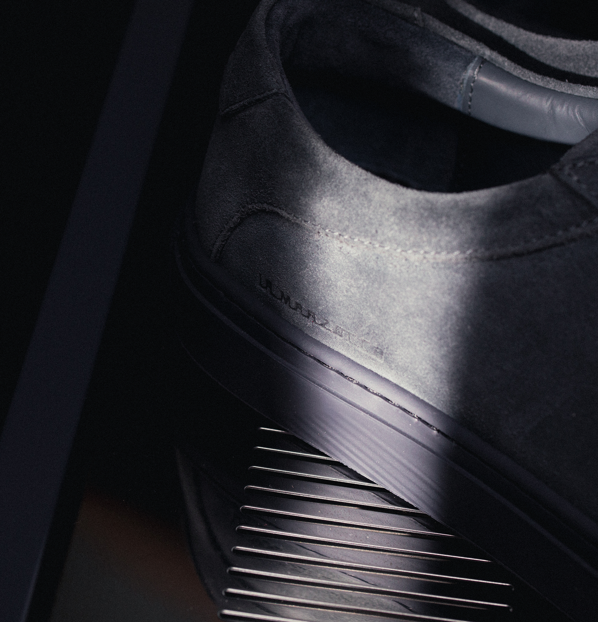 Close-up view of men’s grey suede low-top sneaker Capri showcasing textured suede upper and rubber sole on espresso machine grate