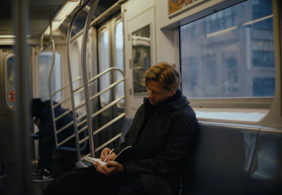 Person writing in a notebook while riding a subway train