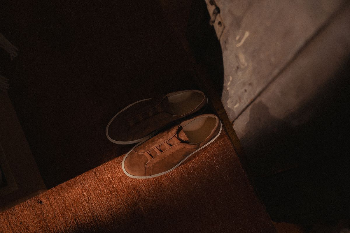 Top-down view of brown suede sneakers showcasing their texture on a sunlit carpet beside dark clothing