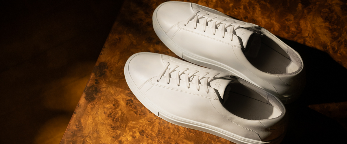 Top-down view of white low-top sneakers showcasing tonal laces and rubber soles on a dark wood table