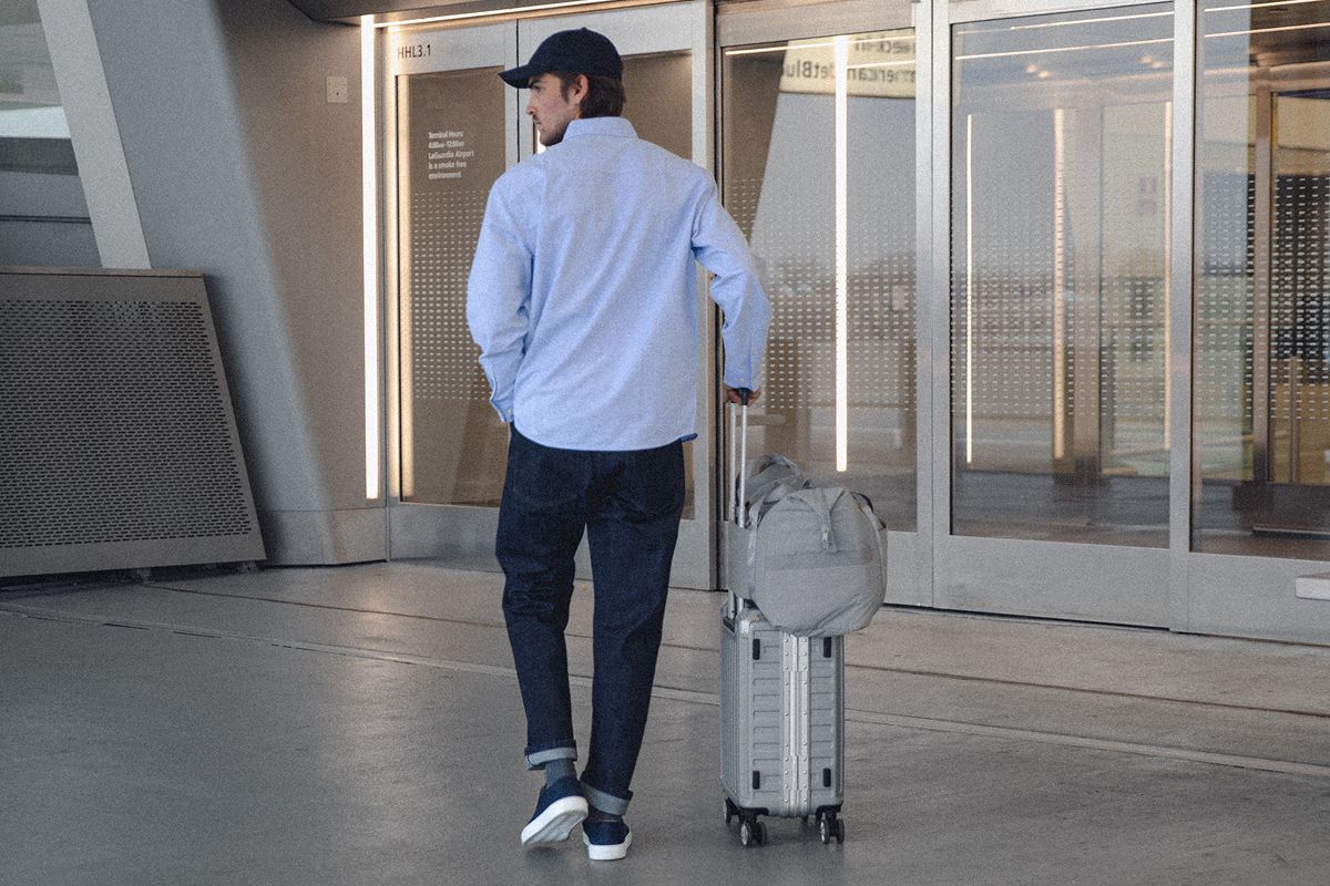 Man in jeans and casual Capri sneakers walking through an airport with a rolling suitcase
