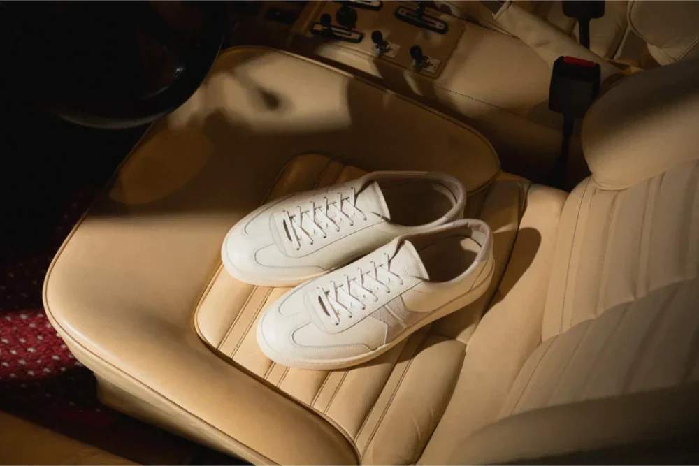 Overhead view of Koio Monza low-top sneakers showcasing white uppers on a tan car seat