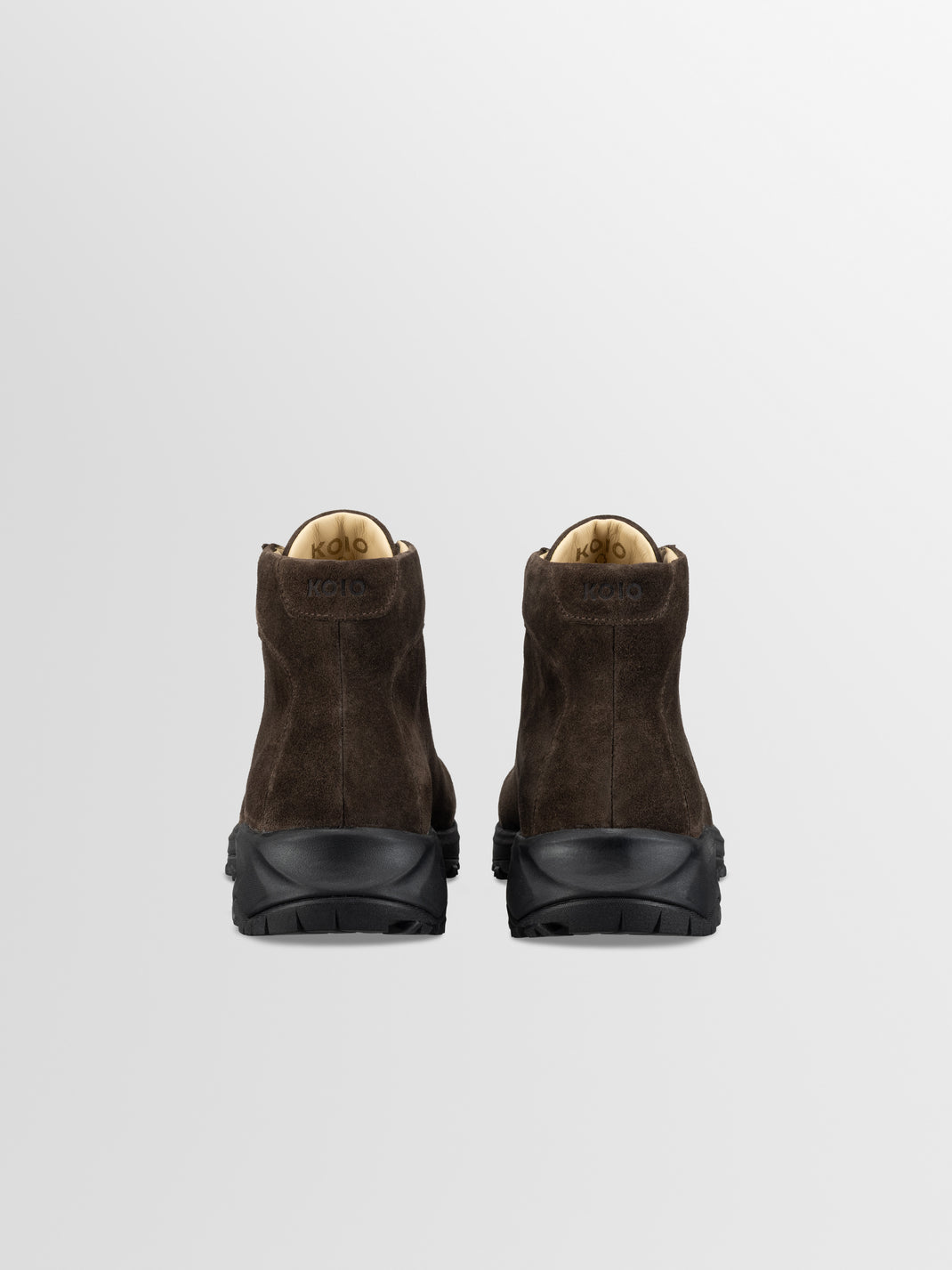 Rear view of Aosta in Cacao boots showcasing brown suede uppers and rugged Vibram black soles on a light gray background