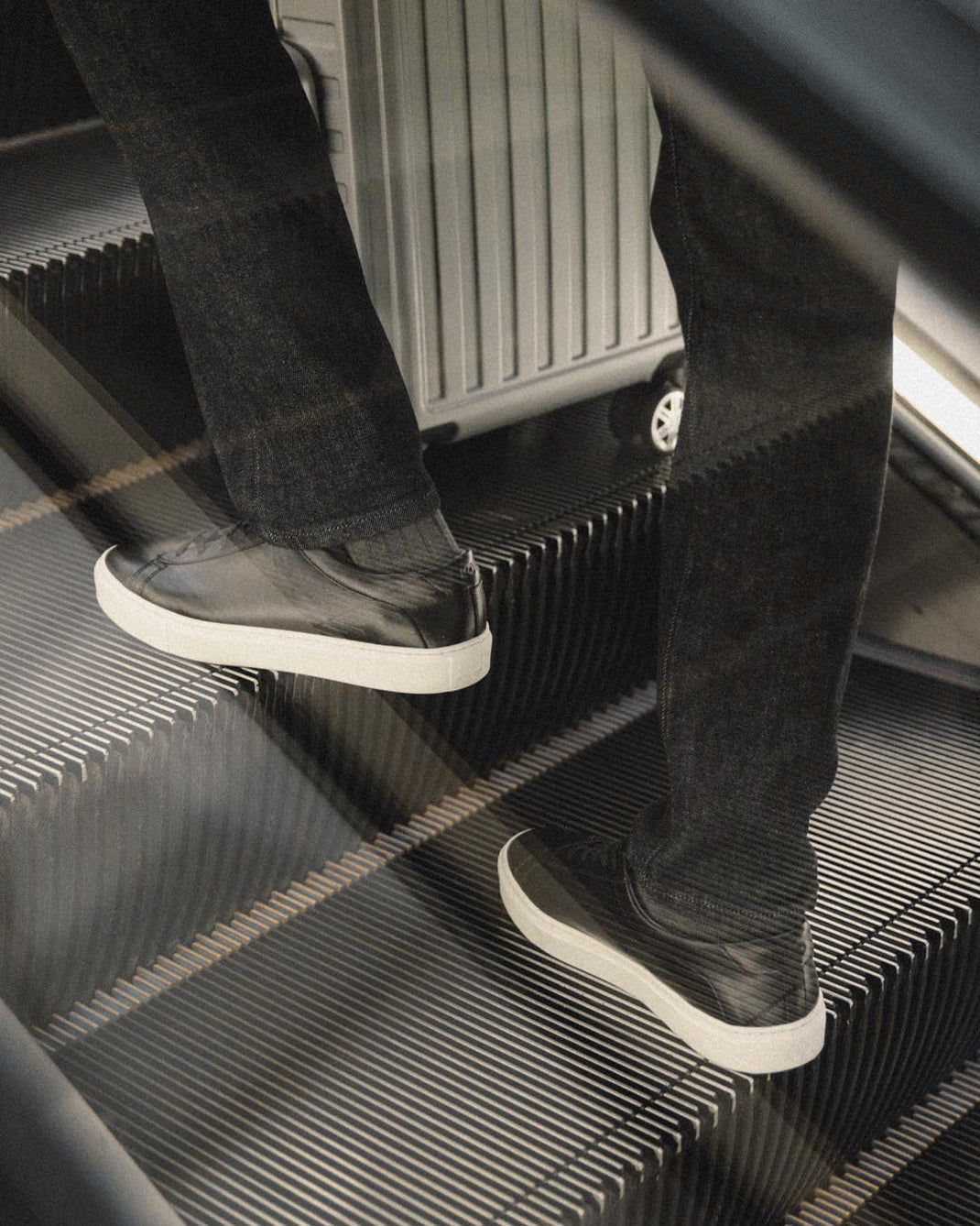Black leather Capri low-top sneakers worn while walking up an escalator