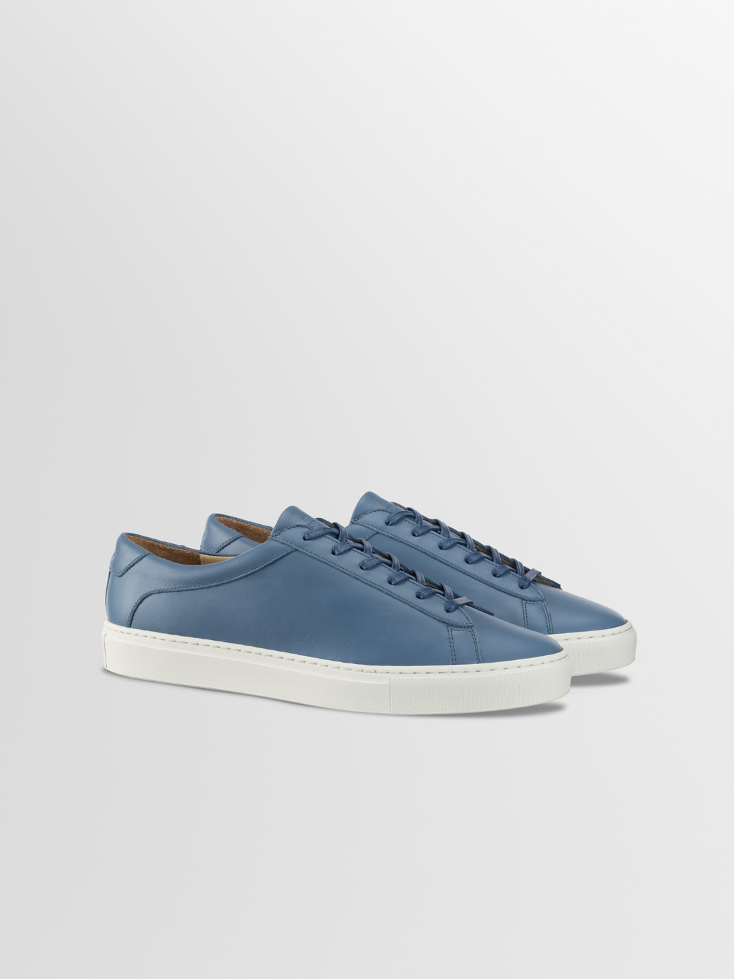 Three-quarter view of Capri in Bay low-top sneakers showcasing blue leather uppers and white rubber soles on a light gray background