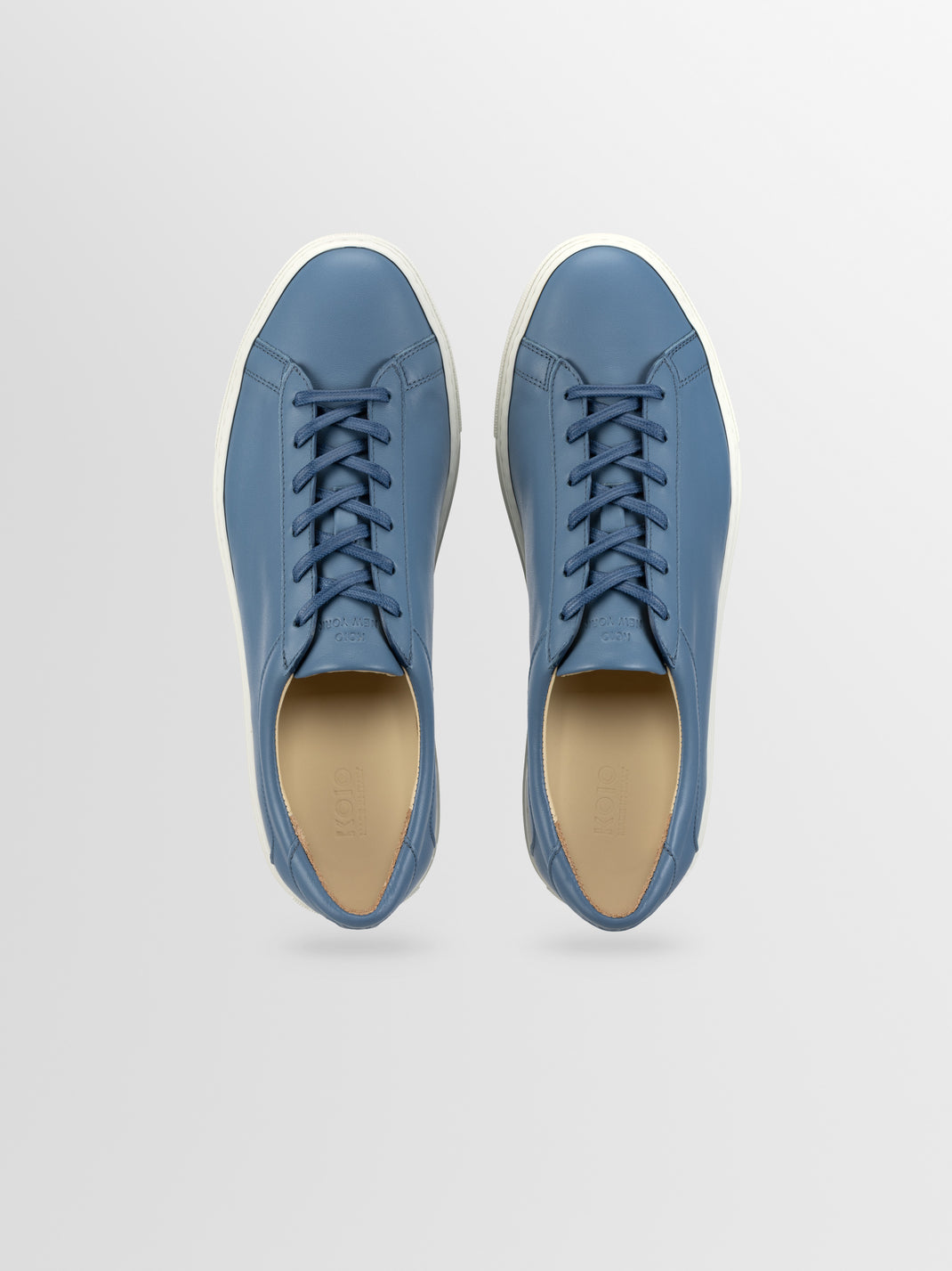 Top view of Capri in Bay men’s blue leather low-top sneakers showcasing lace-up design and white rubber soles on a light gray background