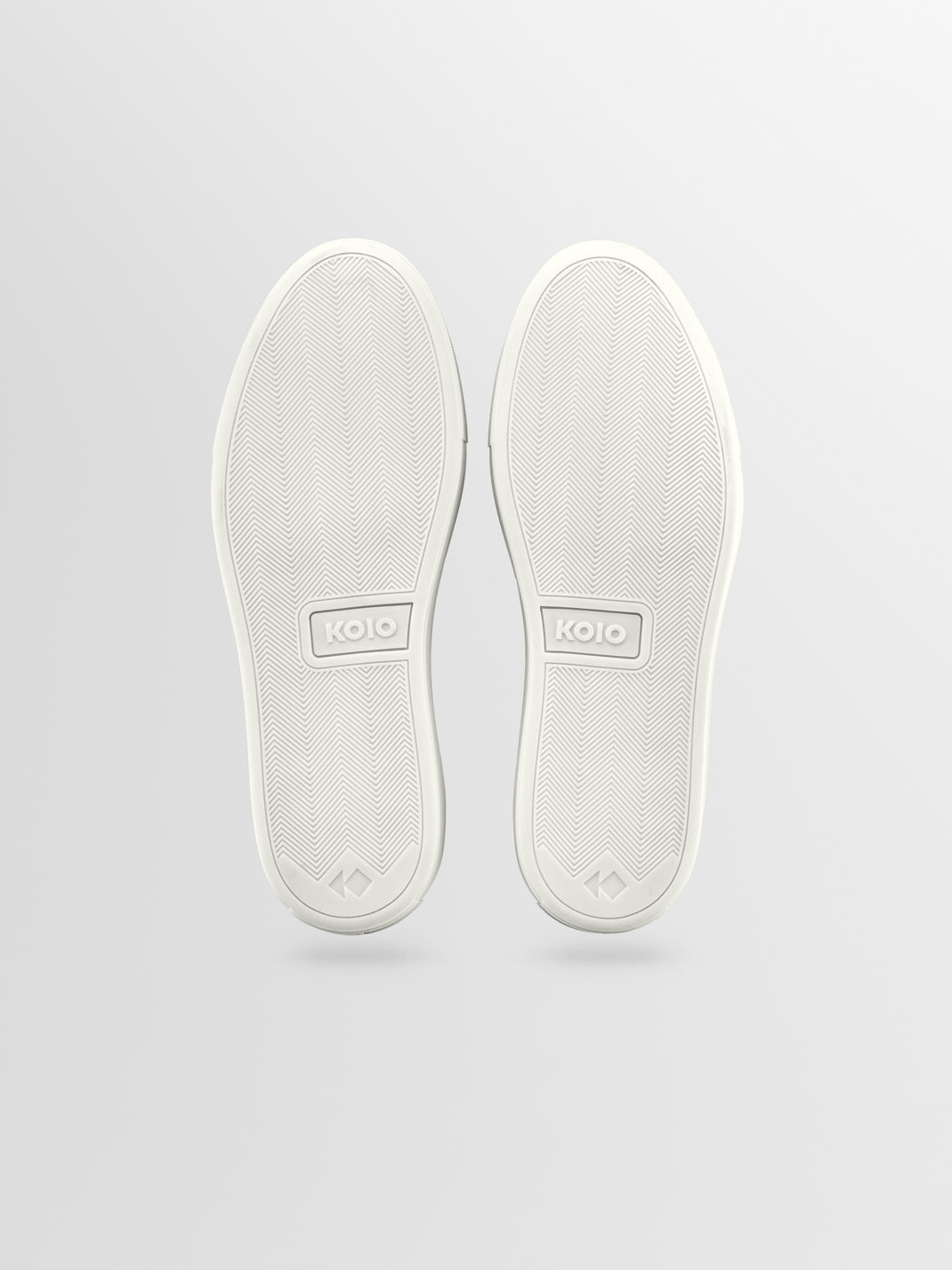 Bottom view of Capri in Bay low-top sneakers showcasing herringbone rubber soles and KOIO logos on a light gray background