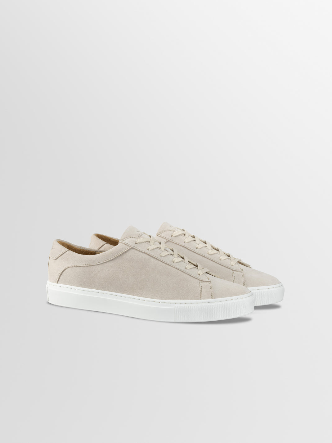 Three-quarter view of men’s Capri in Ivory low-top sneakers with cream suede uppers and white rubber soles on a gray background