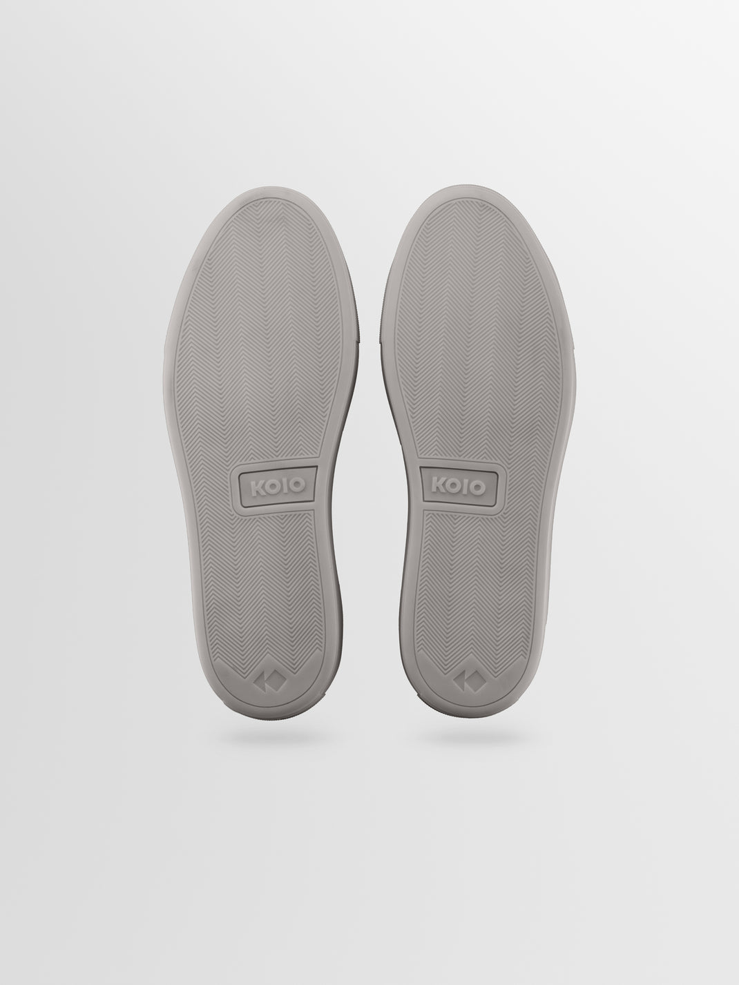 Bottom view of men’s Capri low-top sneakers in Mineral showcasing patterned rubber soles and KOIO logos on a light gray background