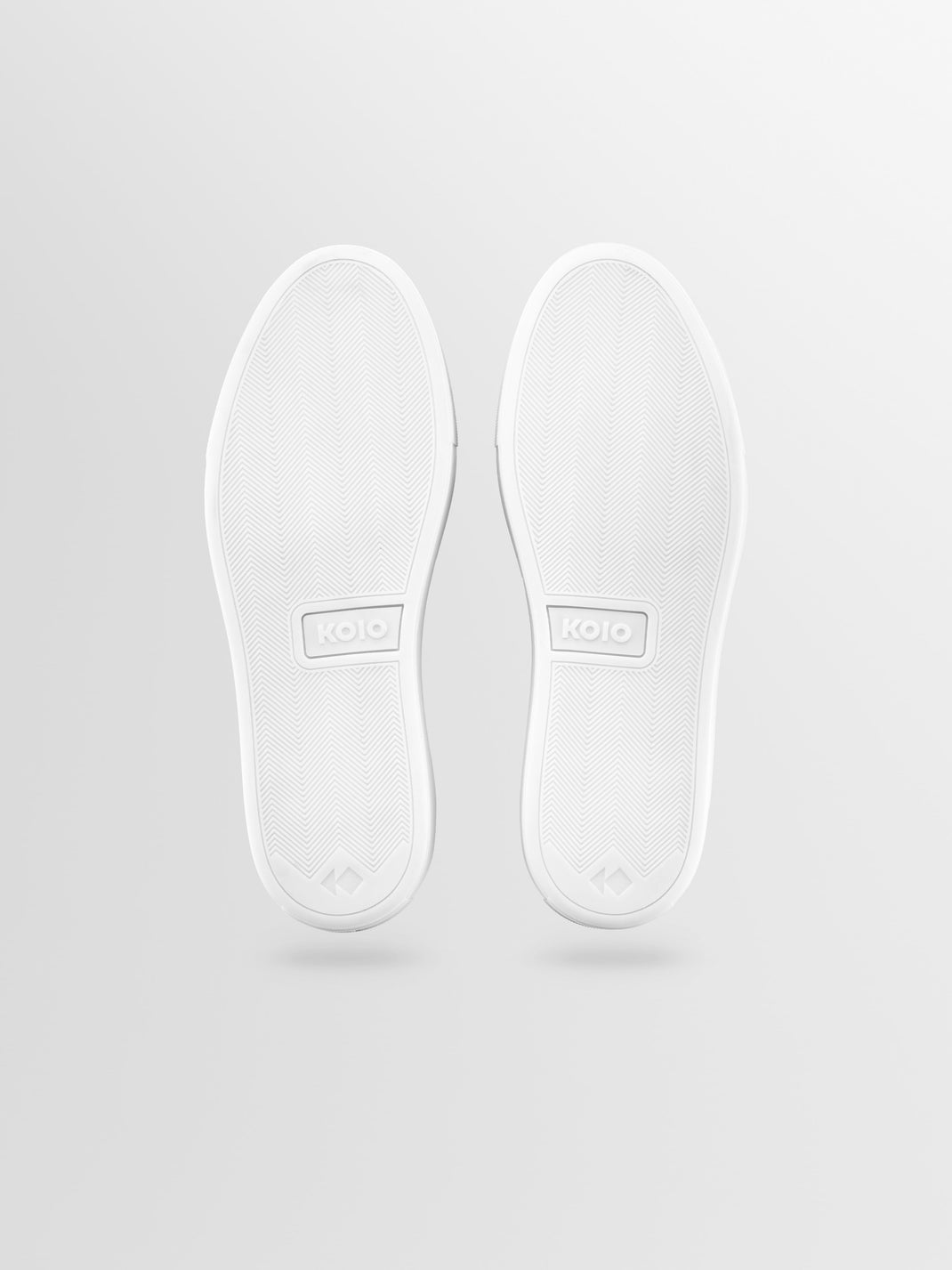 Underside view of Capri leather low-top sneakers in Onyx showcasing herringbone tread and KOIO branding against a light gray background