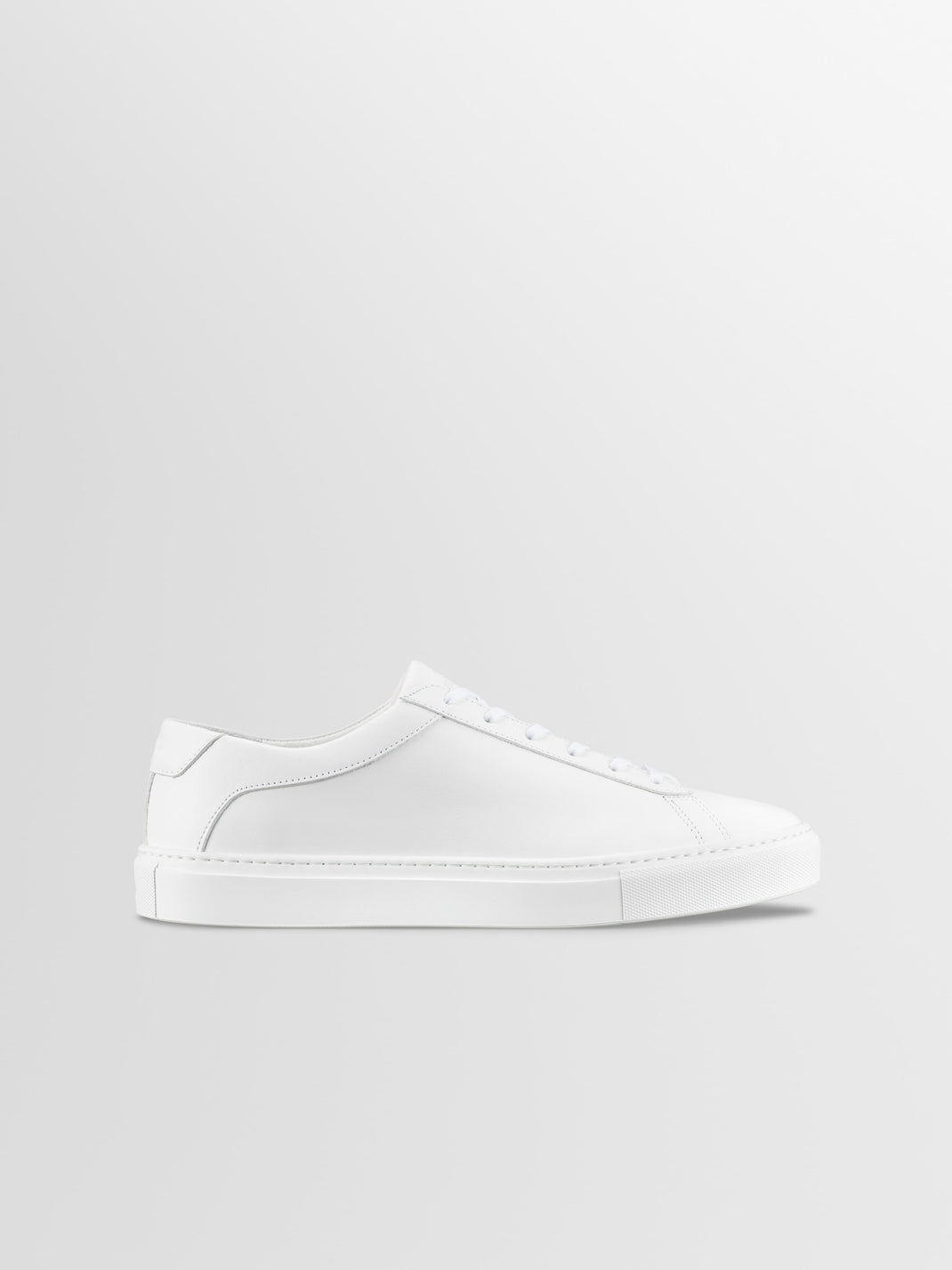 Side view of Capri Triple White low-top sneaker showcasing minimalist silhouette, tonal laces, and rubber sole on light gray background