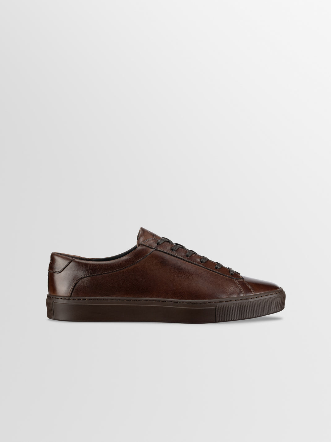 Side view of men’s brown leather low-top sneaker showcasing lace-up details with a light gray background