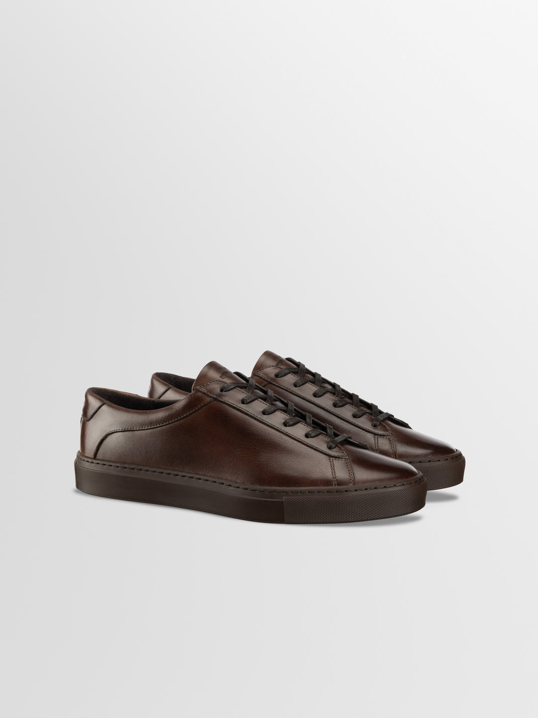Three-quarter view of Capri low-top sneakers in Antica Caffe brown leather showcasing lace-up styling with a light gray studio background