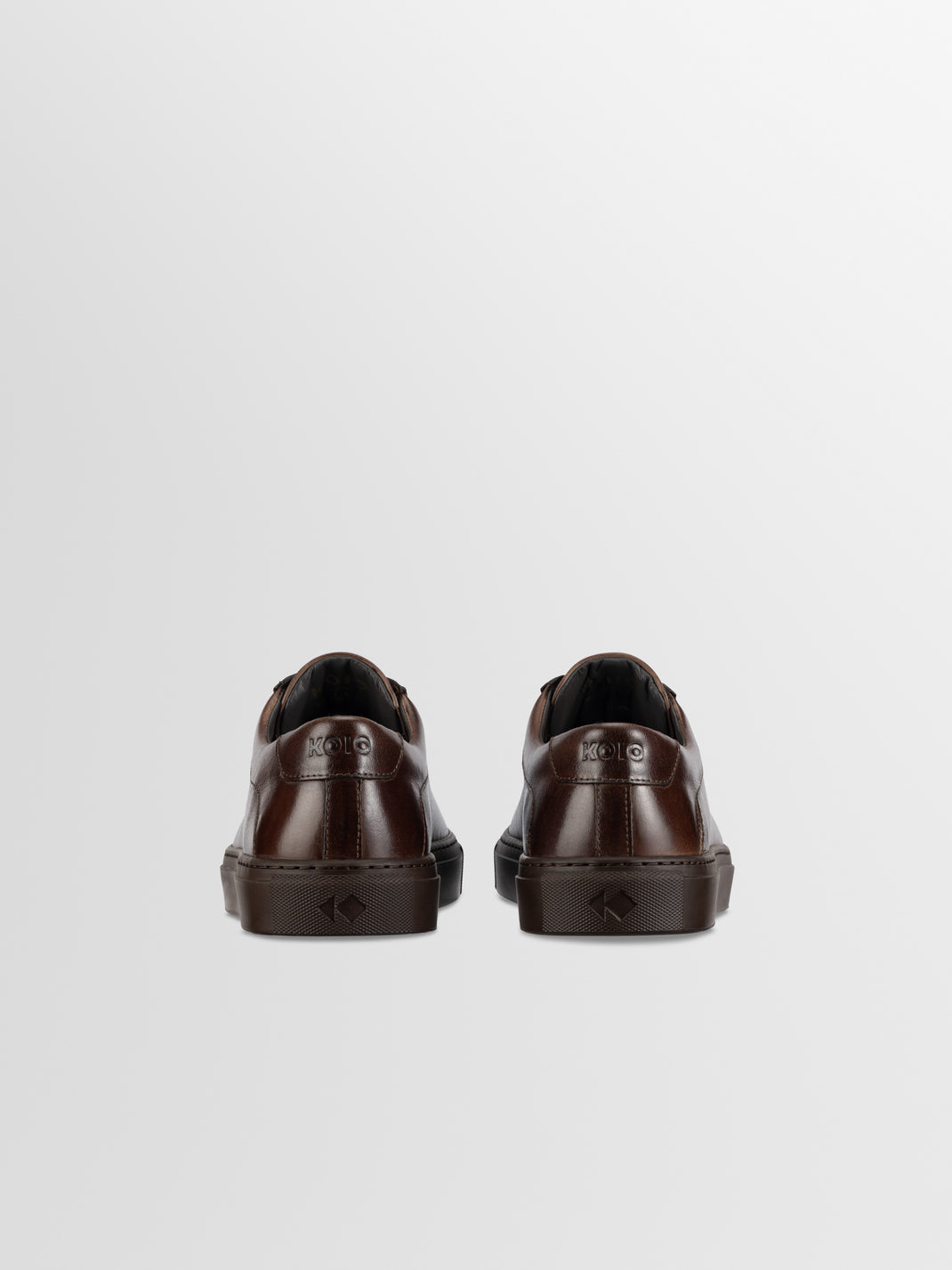 Rear view of brown leather low-top sneakers showcasing branded heels and rubber soles against a light gray background