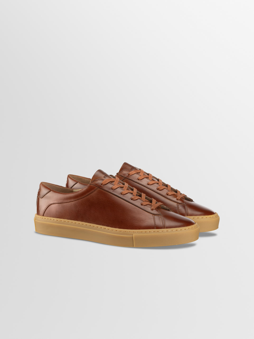Three-quarter view of Capri in Antica Castagna men’s brown leather low-top sneakers showcasing lace-up fronts and gum rubber soles with a light gray background