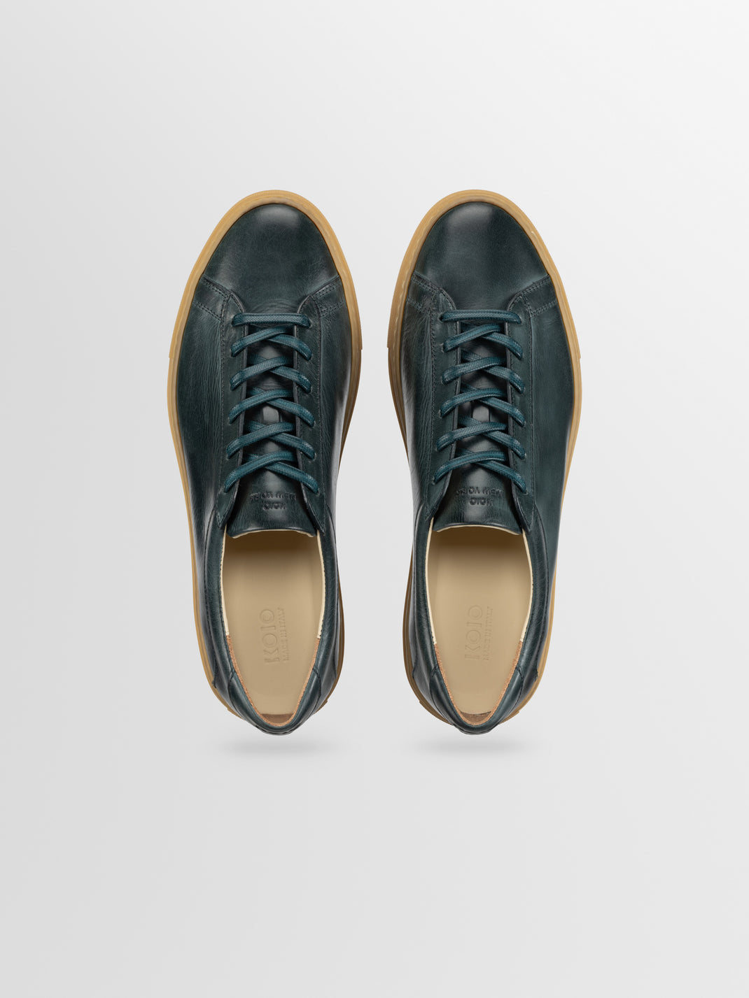 Top view of Capri low-top sneaker in Antica Forest dark green leather, with laces and tan rubber sole on light gray background