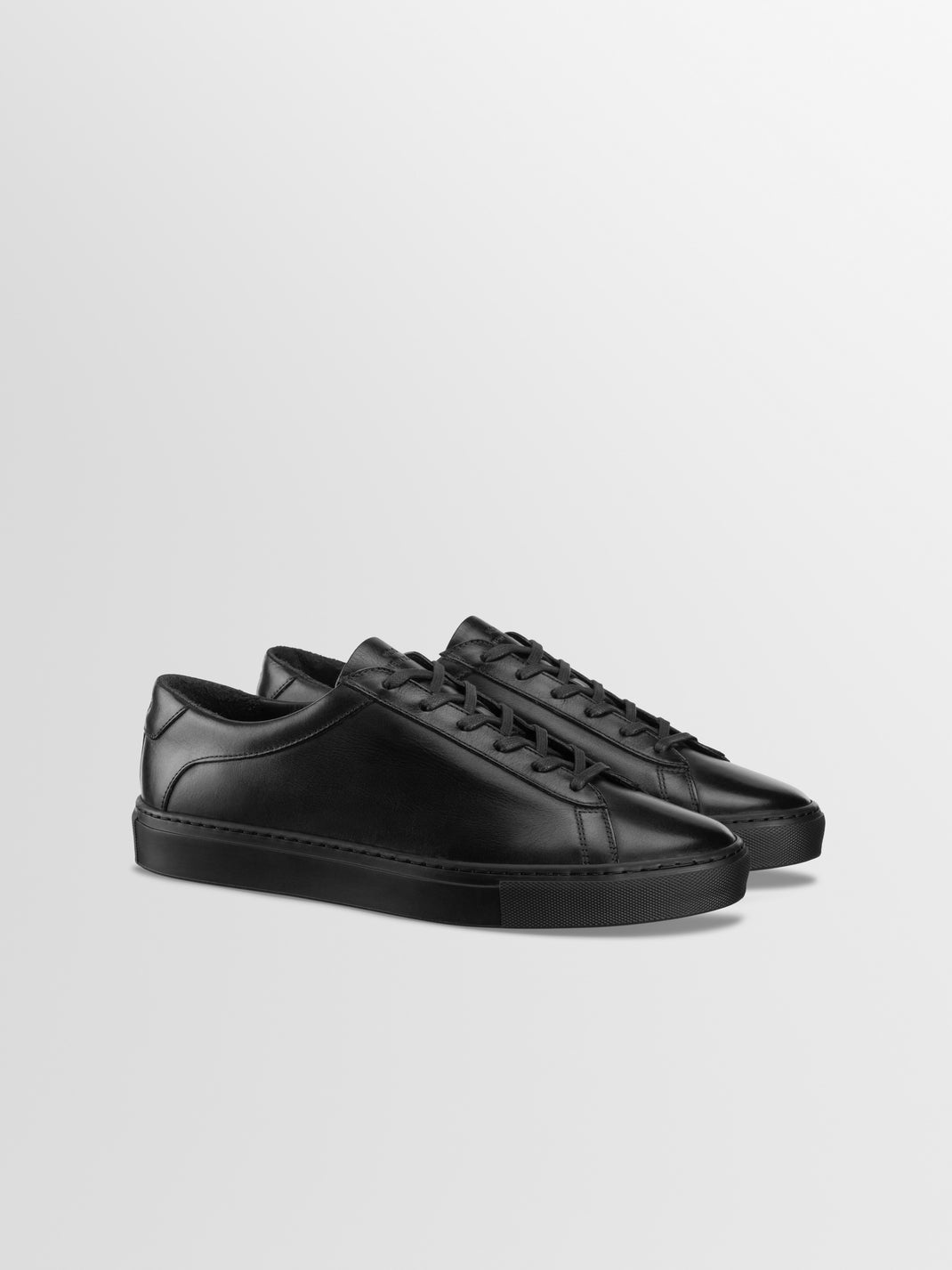 Front three-quarter view of Capri in Antica Nero black leather low-top sneakers showcasing lace-up styling and rubber soles with a light gray background