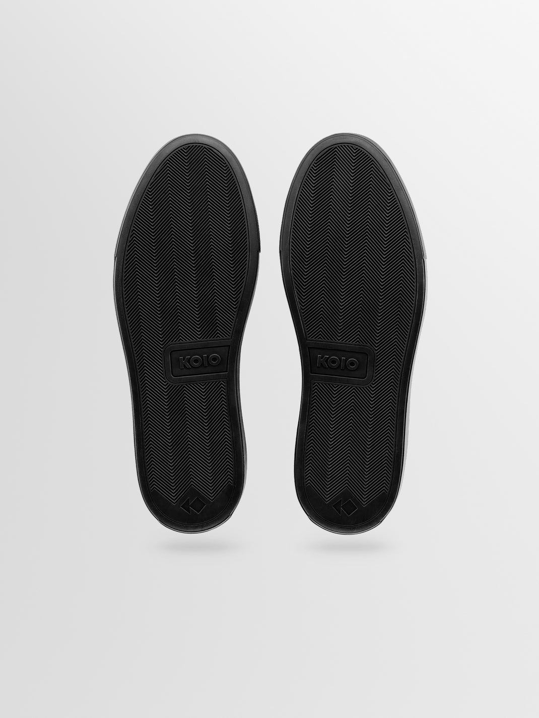 Bottom view of Capri in Antica Nero low-top sneakers showcasing herringbone rubber soles against a light gray background