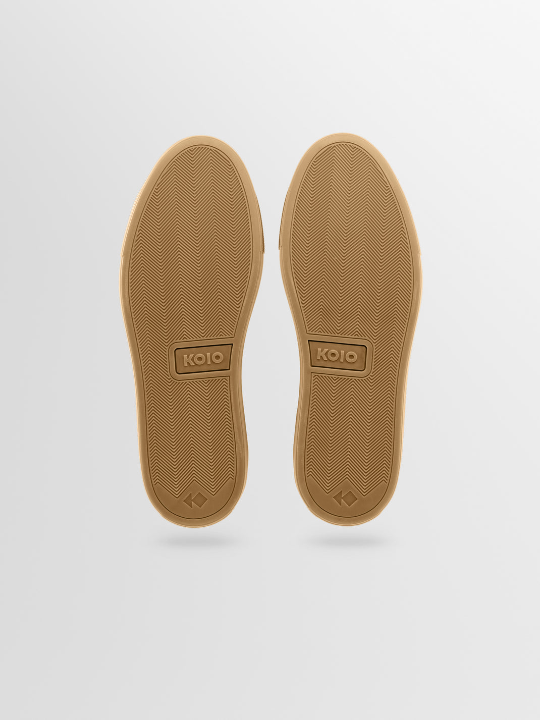 Outsole view of men’s beige leather low-top sneakers showcasing herringbone rubber soles with a light gray background