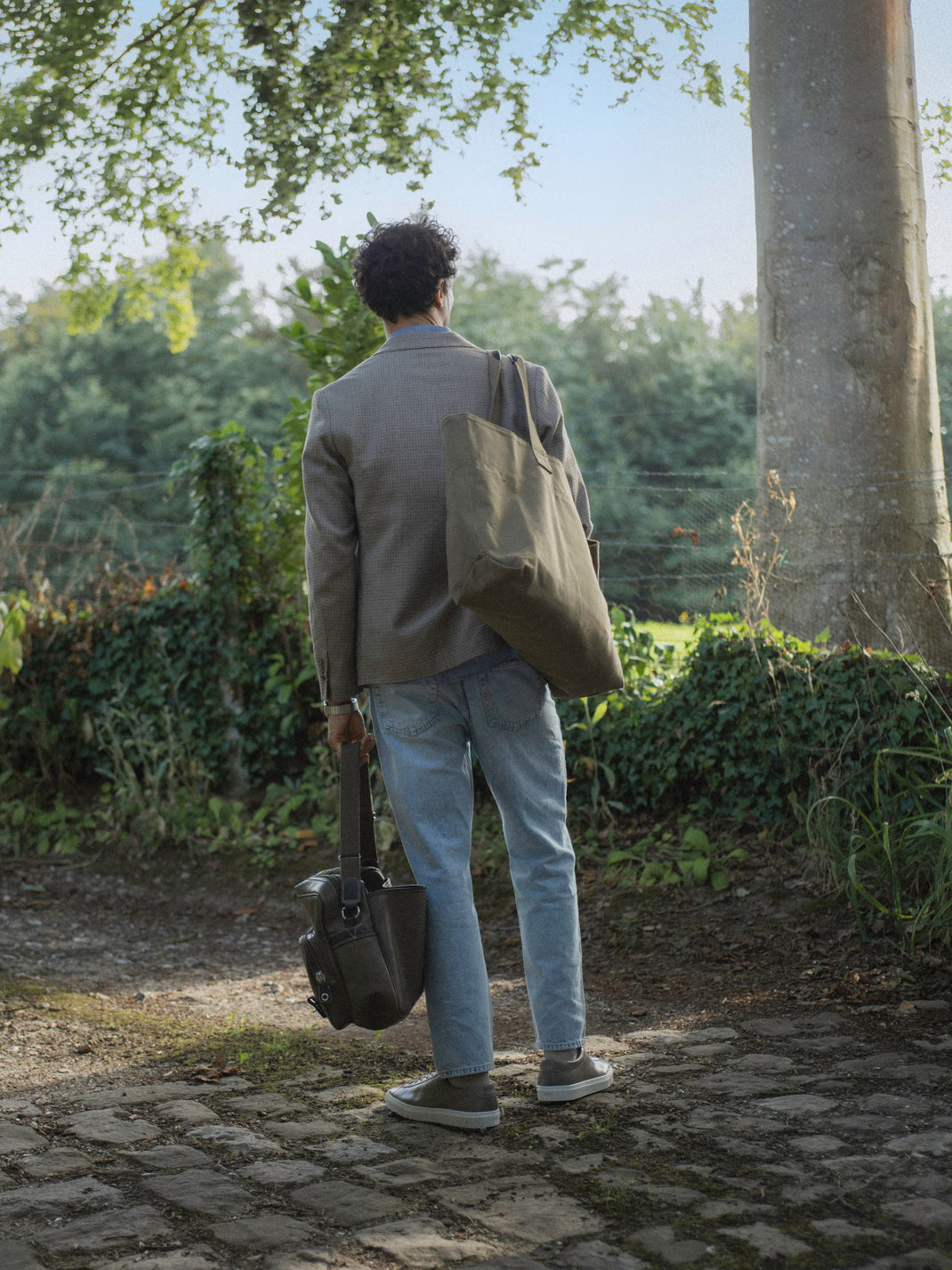Man wearing taupe Capri low-top sneakers while walking on a sunlit garden path