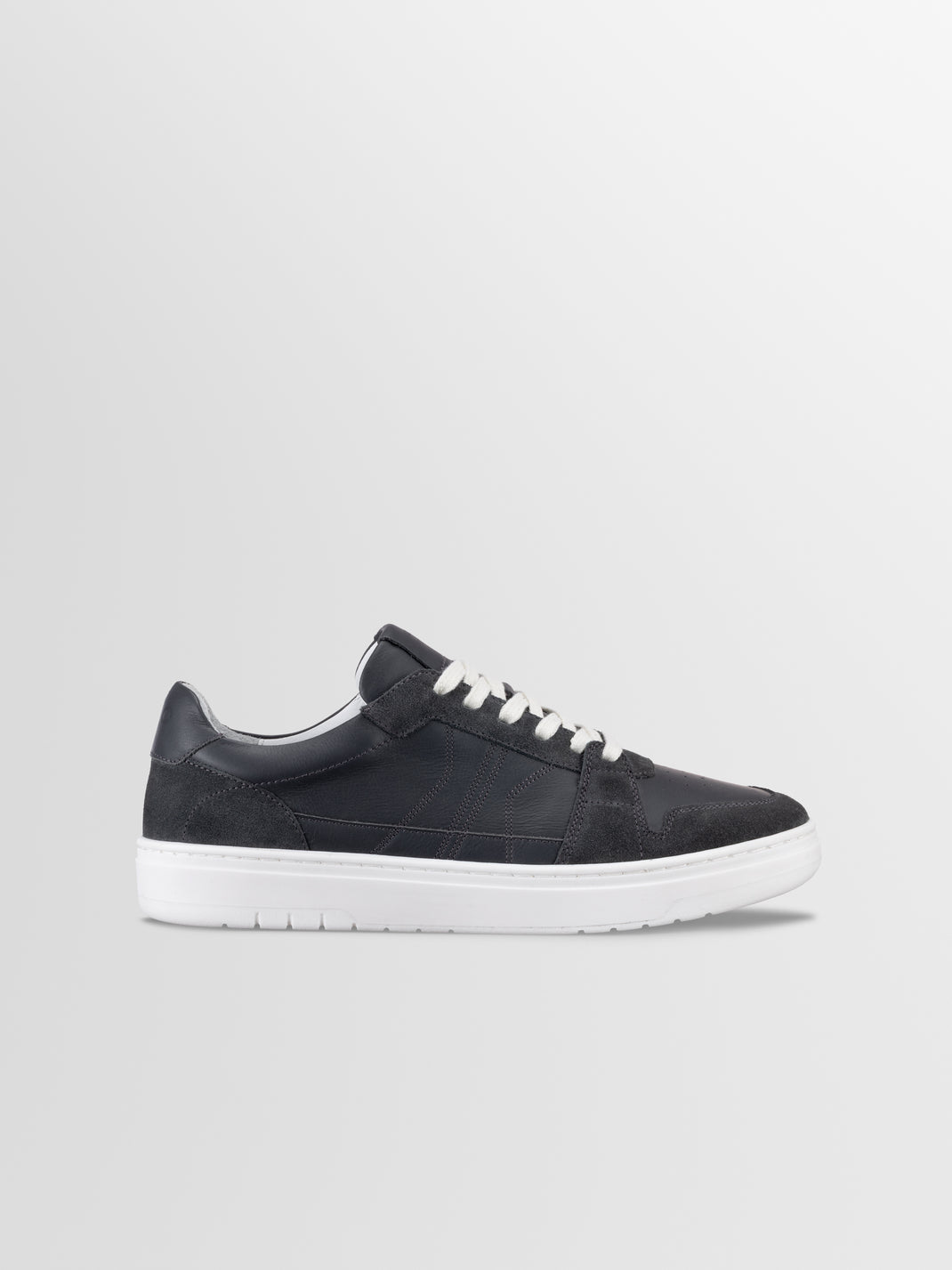Side view of Carrara in Basalt low top sneaker showcasing black suede panels, white laces, and white rubber sole on a light gray background