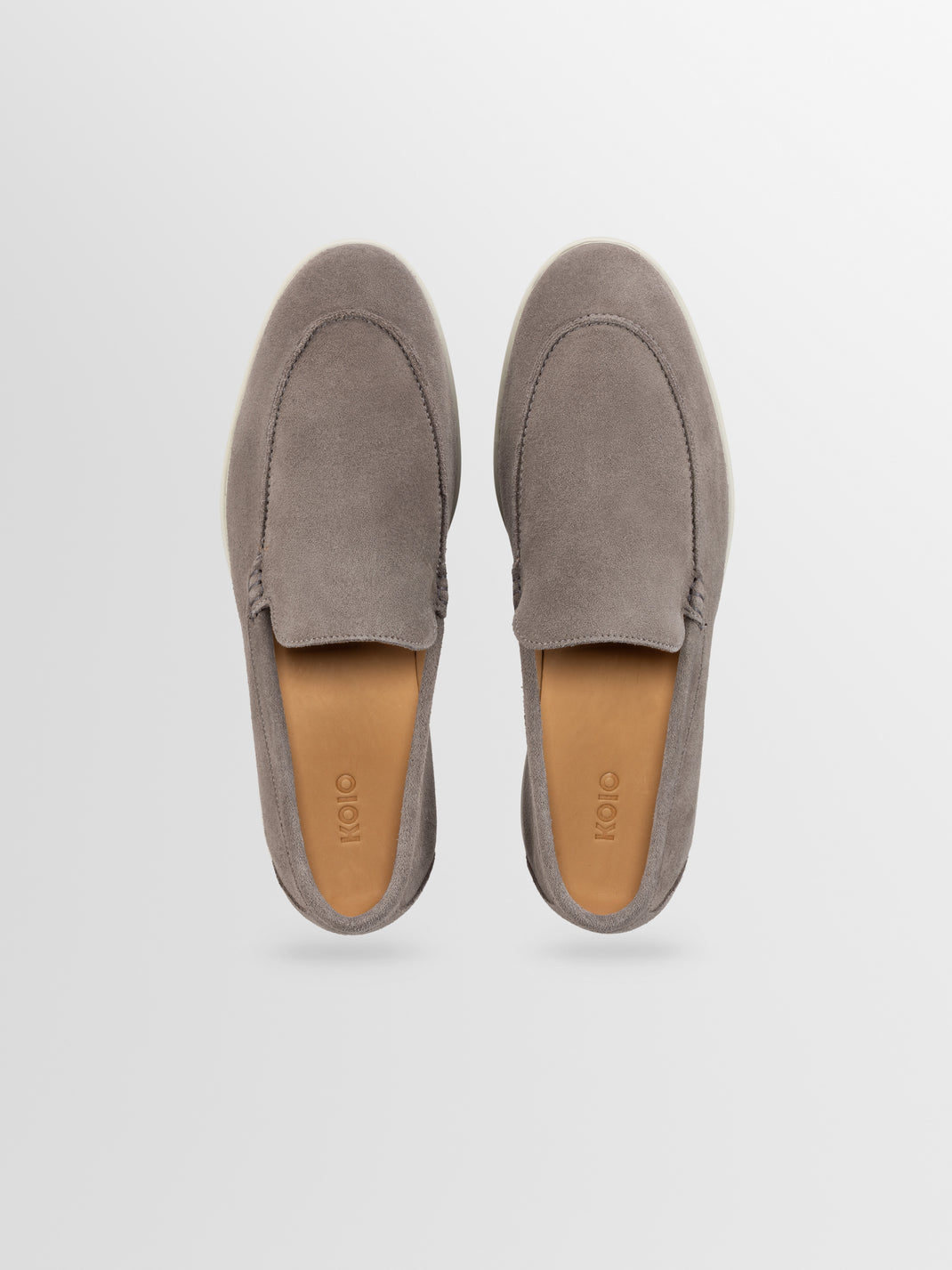 Top view of Catania suede slip-on loafers in taupe showcasing moc-toe stitching and leather footbeds on a light gray background