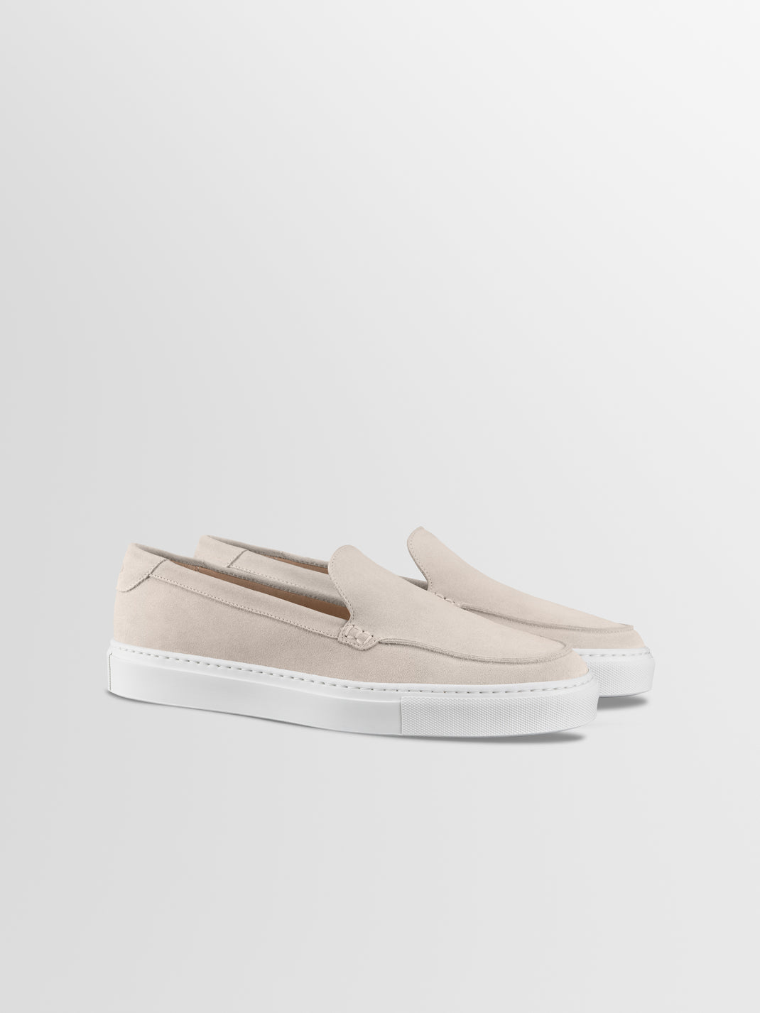Front three-quarter view of men’s Lido ivory suede slip-on loafers showcasing white rubber soles on a light gray background