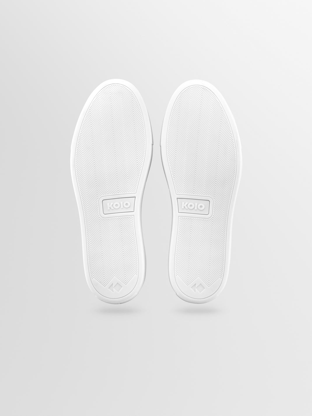 Bottom view of Lido Walnut suede slip-on loafers showcasing textured herringbone soles and KOIO branding on a light gray background