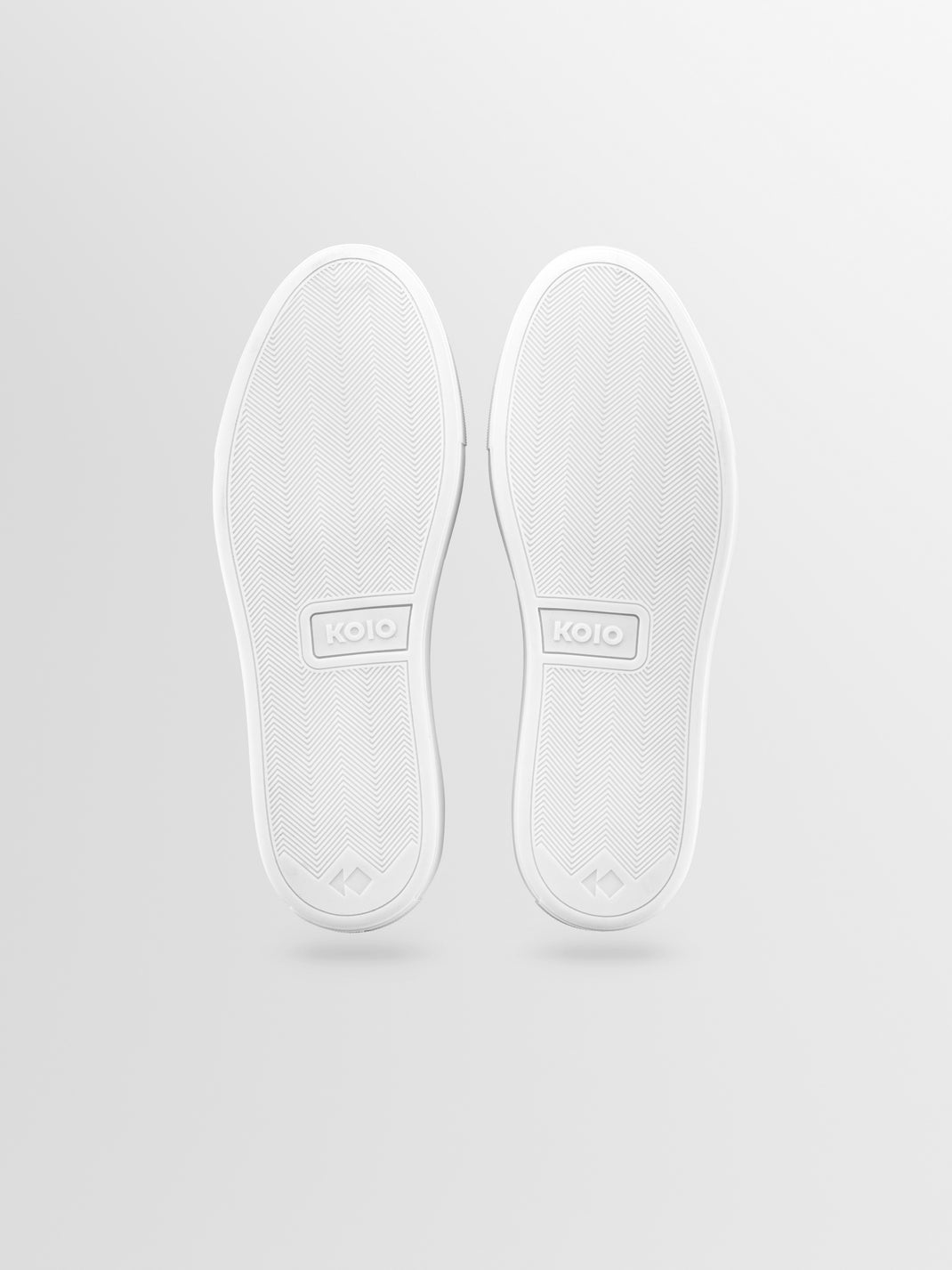 Bottom view of men’s navy nubuck slip-on loafer showcasing white rubber soles with herringbone tread and KOIO branding on a light gray background