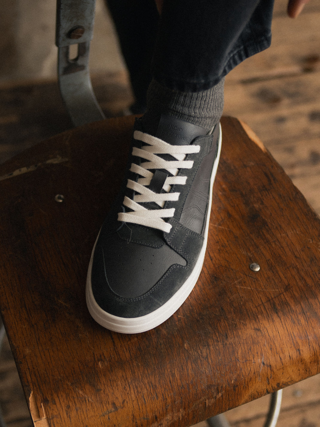 Close-up view of men’s black suede Carrara low-top sneaker with white laces and sole on a wooden table