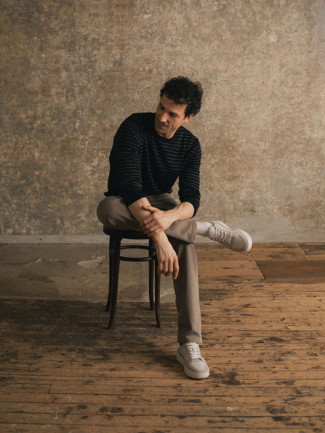 Man sitting on a stool wearing white and beige Carrara suede sneakers in a rustic studio