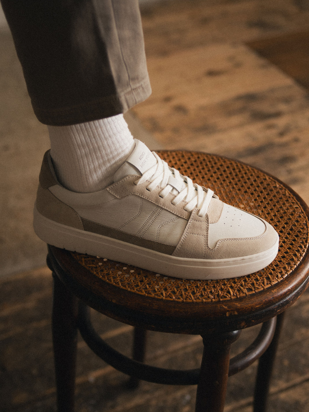 Side view of men’s white and beige suede low-top sneaker showcasing lace-up design on a woven stool