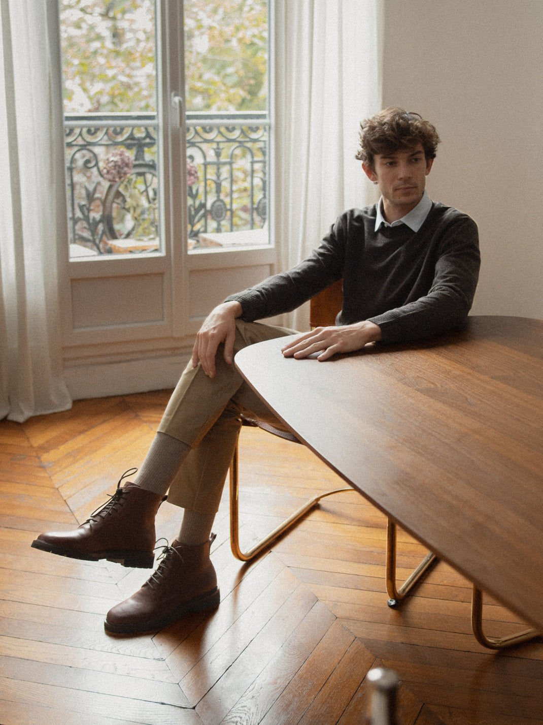 Man wearing brown leather lace-up boots while seated at a table in a bright room