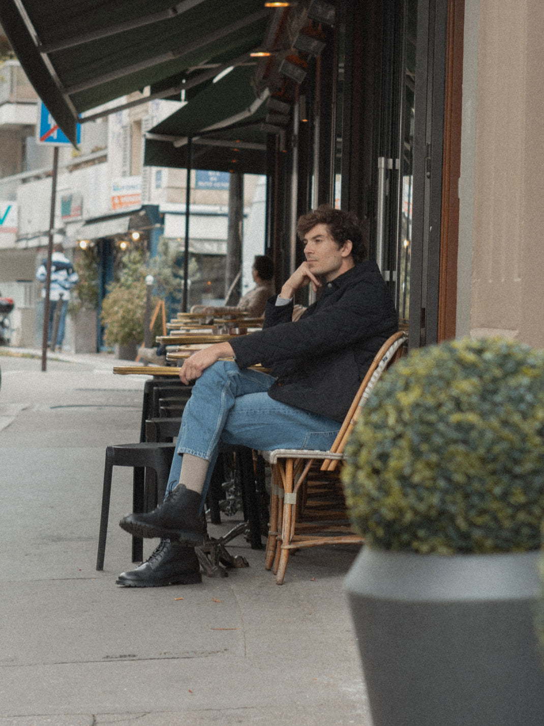 Man seated at a sidewalk café wearing black leather lace-up boots
