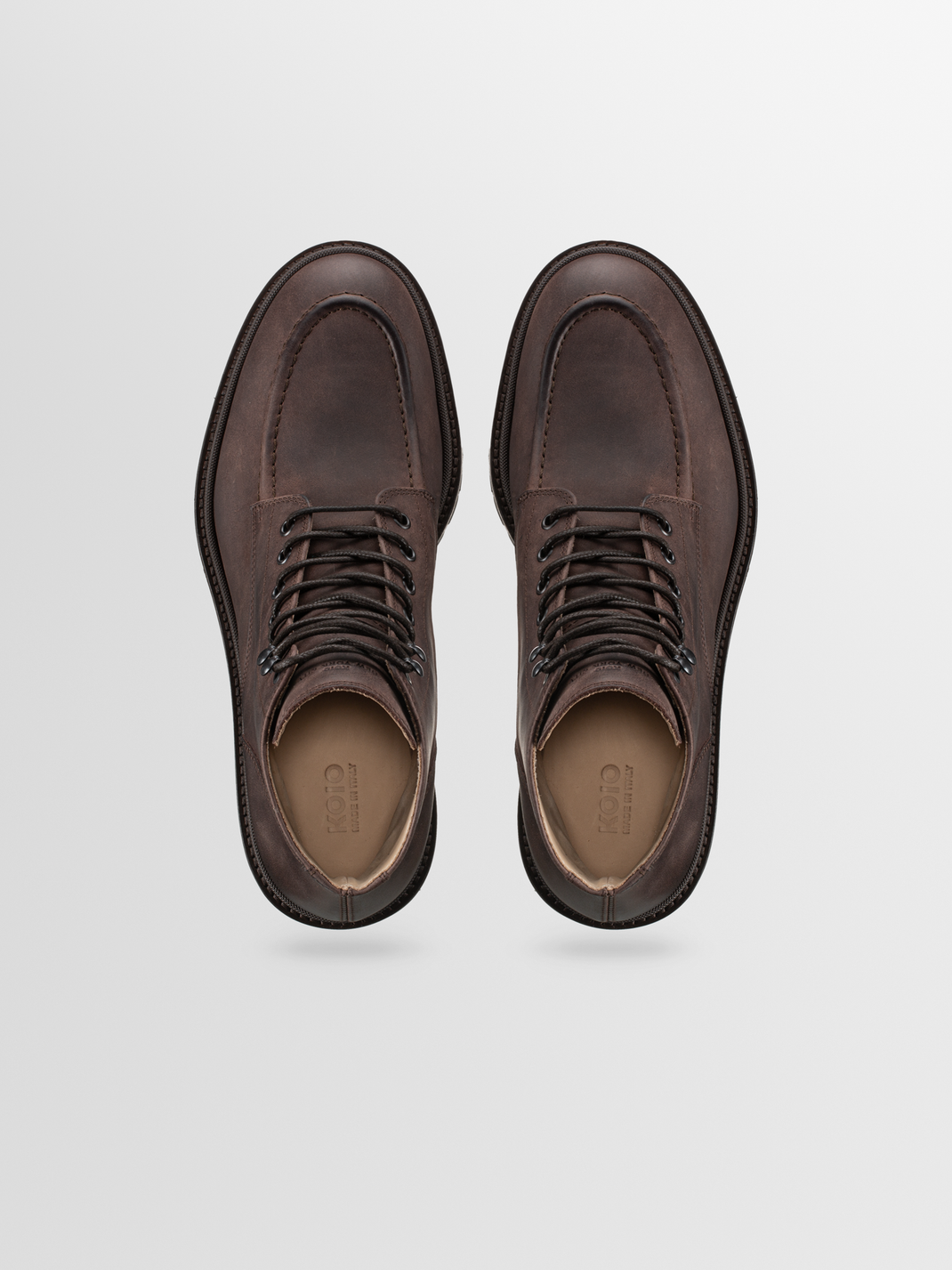 Top view of a pair of Milo leather boots in Chocolate showcasing lace-up fronts and open interiors on a light gray background