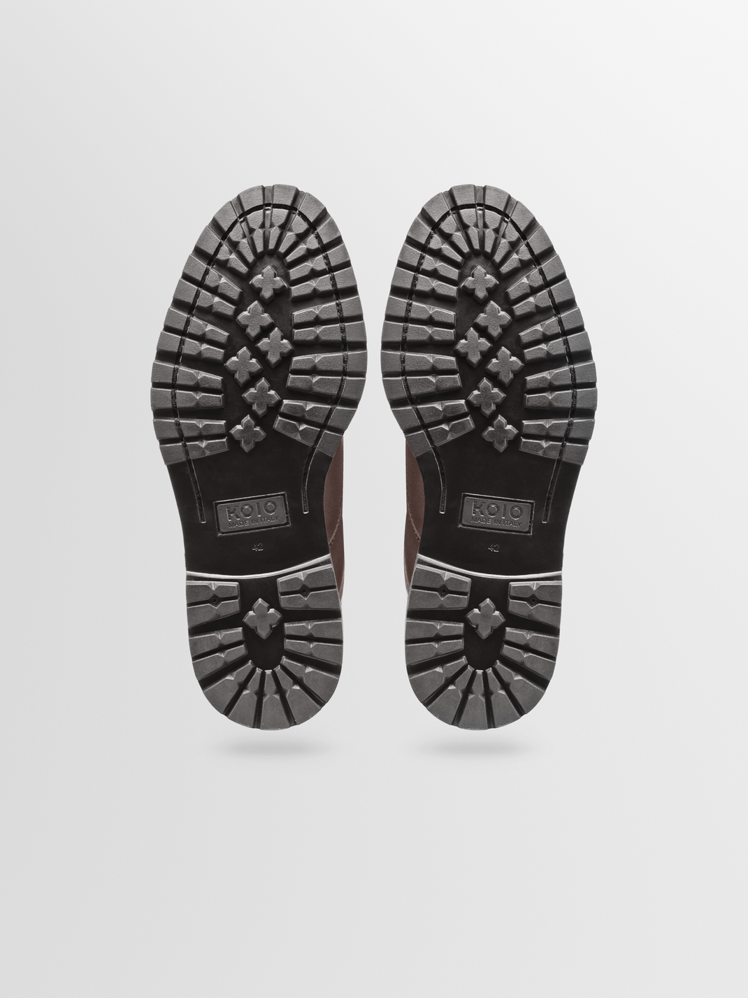 Bottom view of the Milo leather boot in Chocolate showcasing textured rubber soles against a light gray background
