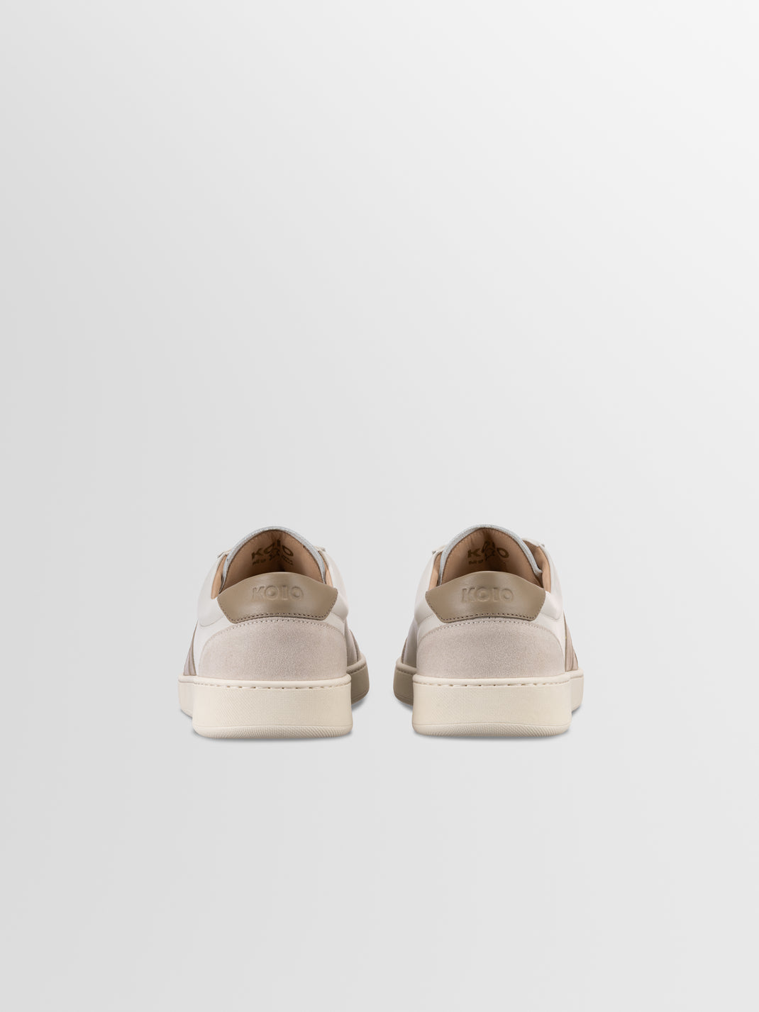 Rear view of Monza leather low-top sneakers in latte showcasing contrasting heel panels and rubber soles on a light gray background