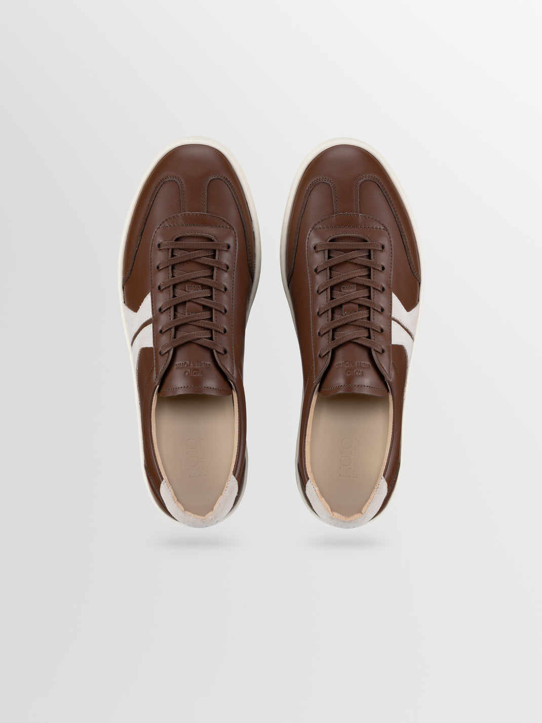 Top view of Monza low-top sneakers in Tobacco brown leather showcasing white side stripes and brown laces on a light gray background