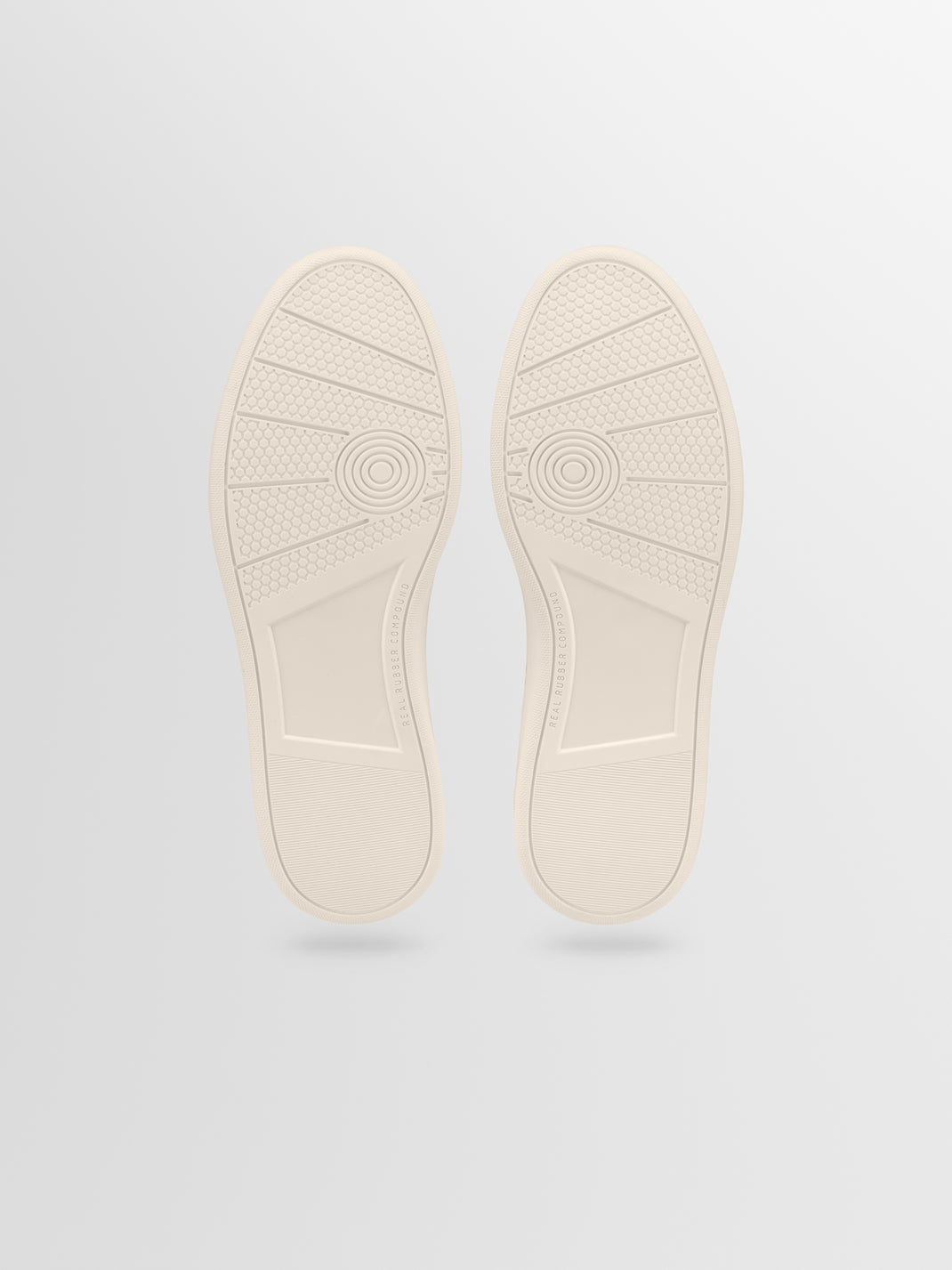 Bottom view of Monza in Tobacco low-top sneakers showcasing textured cream rubber soles on a light gray background