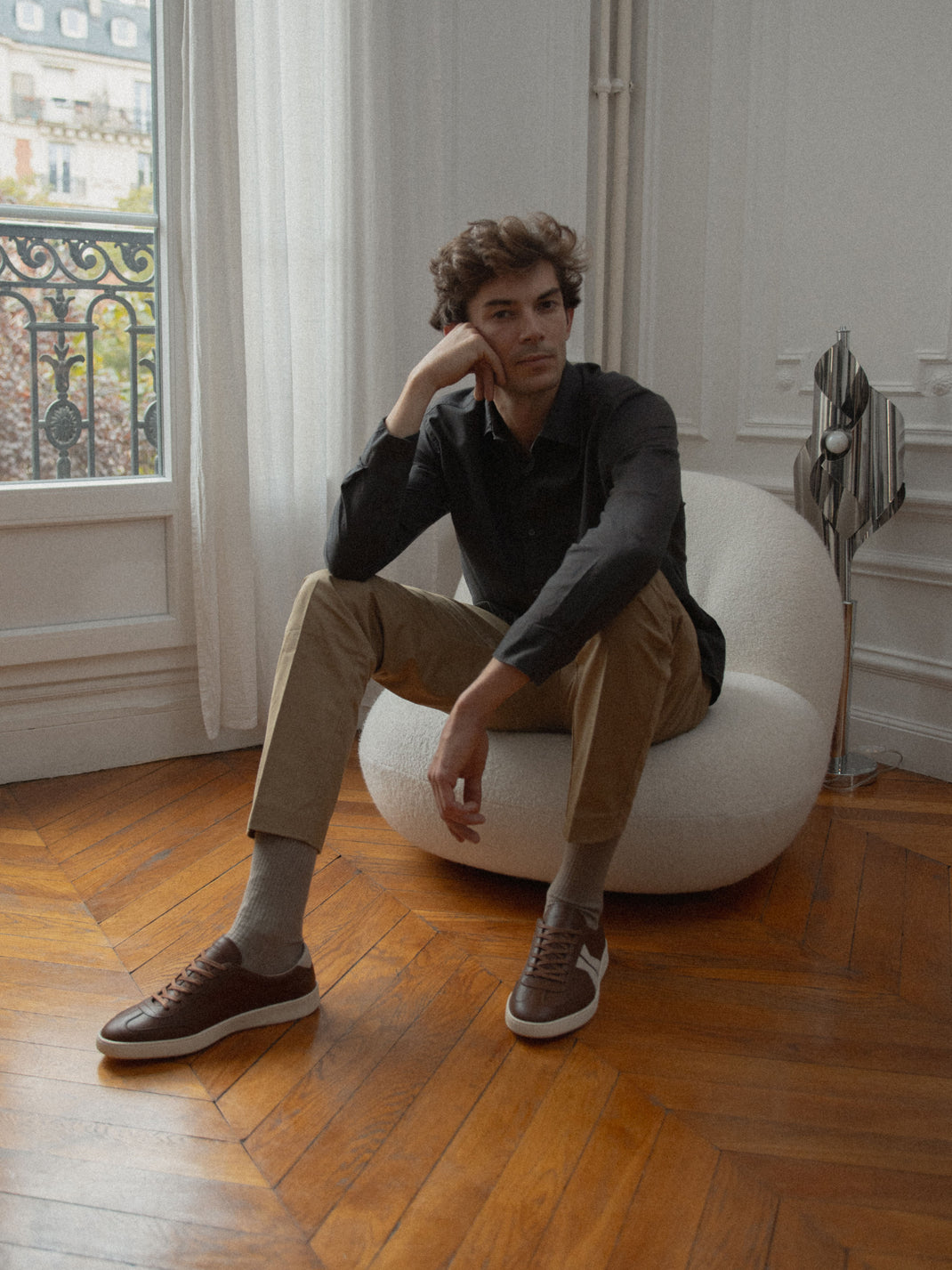 Man wearing brown leather Monza low-top sneakers while seated in a modern room