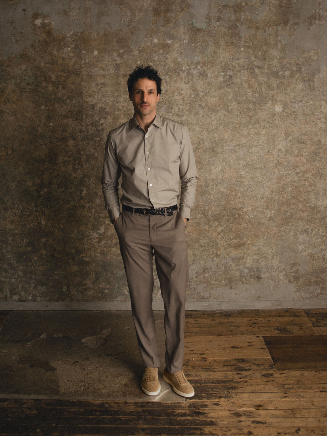 Full-length view of men’s Monza in Wheat low-top sneaker showcasing light brown suede on a model against a textured wall