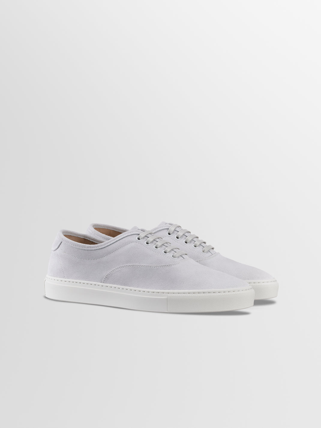 Angled view of Portofino in Cirrus low-top sneakers showcasing white suede uppers and rubber soles against a light gray background