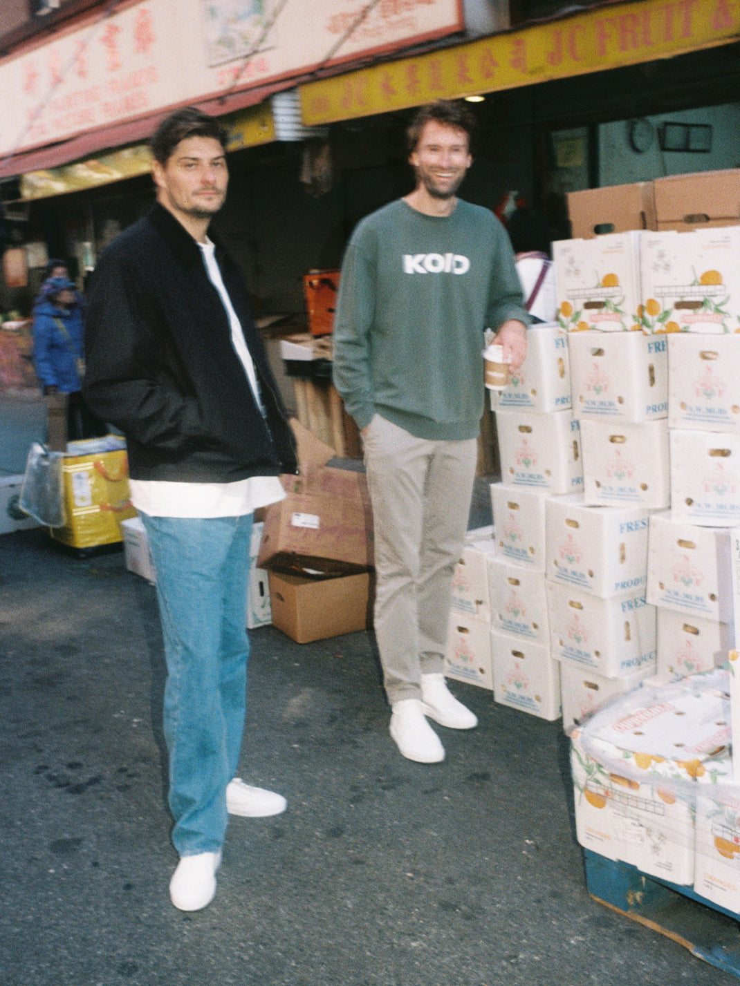 Two men wearing the Capri Triple White leather sneakers at a produce market beside stacked boxes